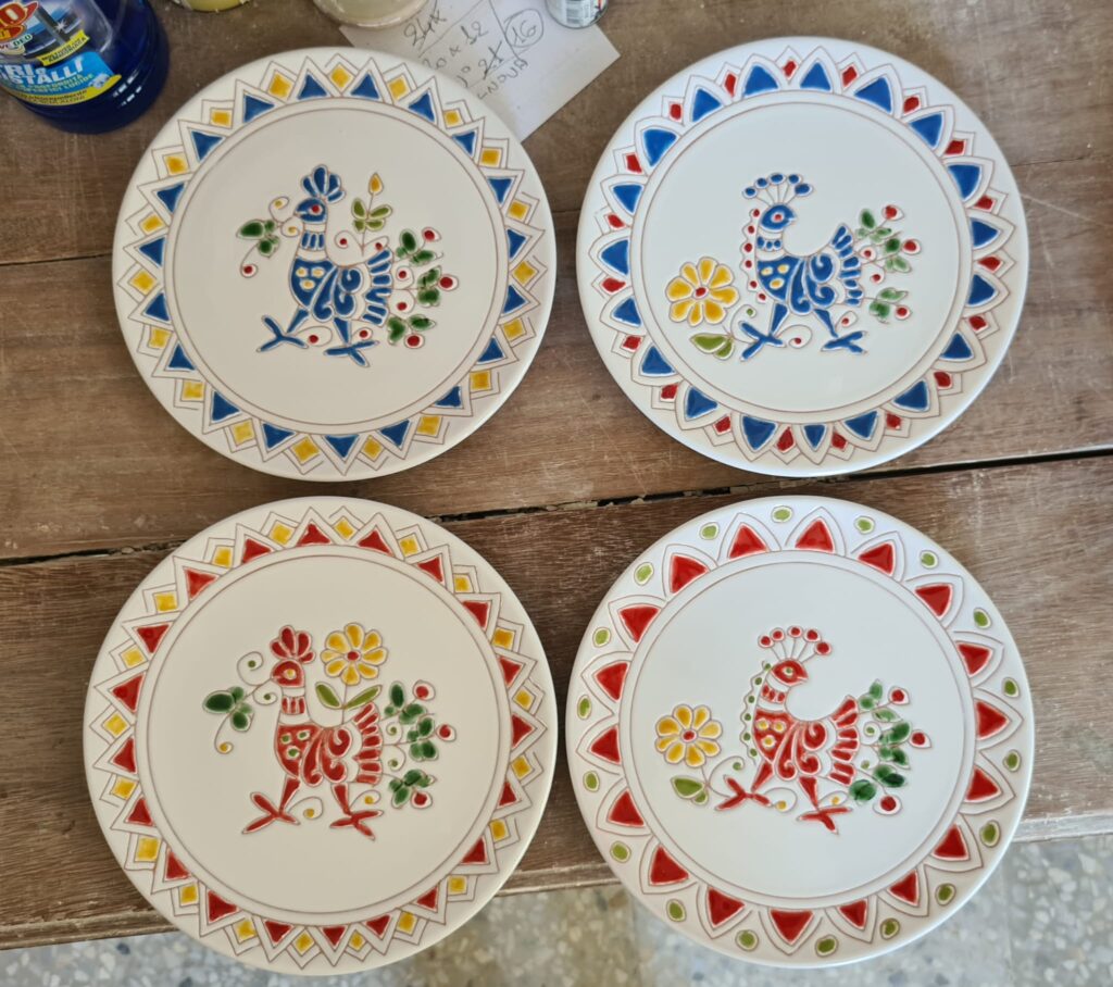 Creazioni artigianali di Andrea Farci: piattini decorati con pavoncelle rosse e azzurre